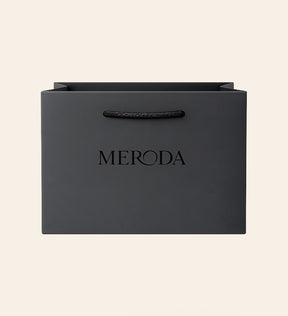 Mattschwarze Geschenktasche mit Kordelgriff und geprägtem Meroda-Logo vor cremefarbenem Hintergrund.