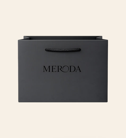 Mattschwarze Geschenktasche mit Kordelgriff und geprägtem Meroda-Logo vor cremefarbenem Hintergrund.