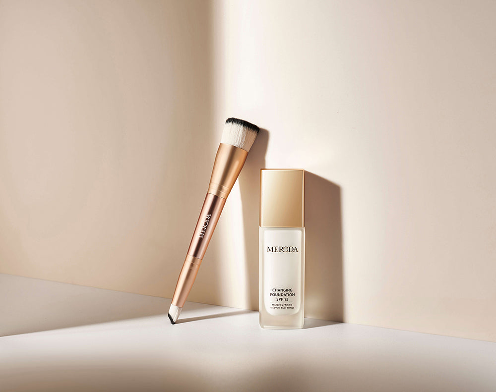 Meroda Cosmetics 2-in-1 Build & Conceal Brush lehnt an der Changing Foundation Flasche