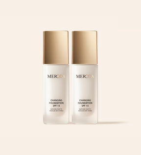 Zwei Meroda Changing Foundation Flakons mit goldenen Kappen nebeneinander auf einem neutralen Hintergrund präsentiert.