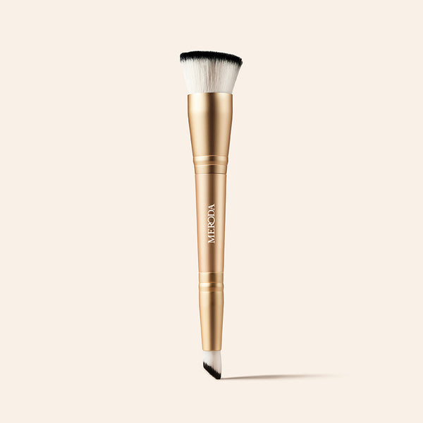 2-in-1 Build & Conceal Brush mit goldenem Griff und zweiseitigen Synthetikborsten auf neutralem Hintergrund.
