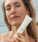 Daily Face SPF 40 Tube gehalten von einem Model mit strahlender Haut in einer sonnigen Strandkulisse.
