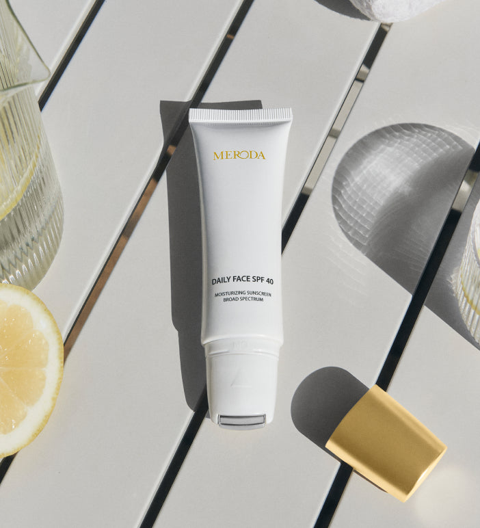 Daily Face SPF 40 Tube mit kühlendem Metall-Rollerball auf einem hellen Tisch neben einer Zitronenscheibe.