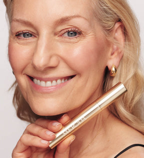 Lächelnde Frau hält die Meroda Cosmetics Gilded Lashes Mascara