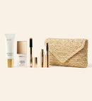 Summer Travel Icons Set mit Daily Face LSF 40, Changing Foundation, Lip Tint, Mascara und einer beigen, gewebten Bast-Clutch.