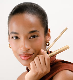 The Brow Defining Duo mit The Precision Brow Pencil und The Precision Brow Gel in Gold, gehalten von einem Model