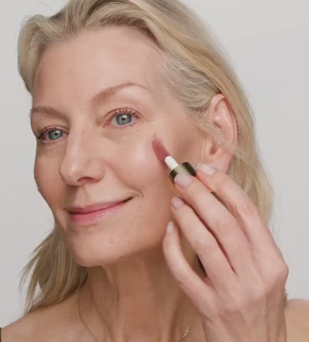 Modell beim Auftragen von cremigem Liquid Blush mit einem Pinsel für einen frischen, natürlichen Teint.
