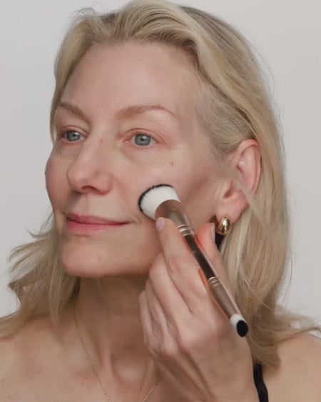 Eine Frau mit hellem Teint verblendet Changing Foundation mit einem 2-in-1-Pinsel für einen natürlichen Glow.